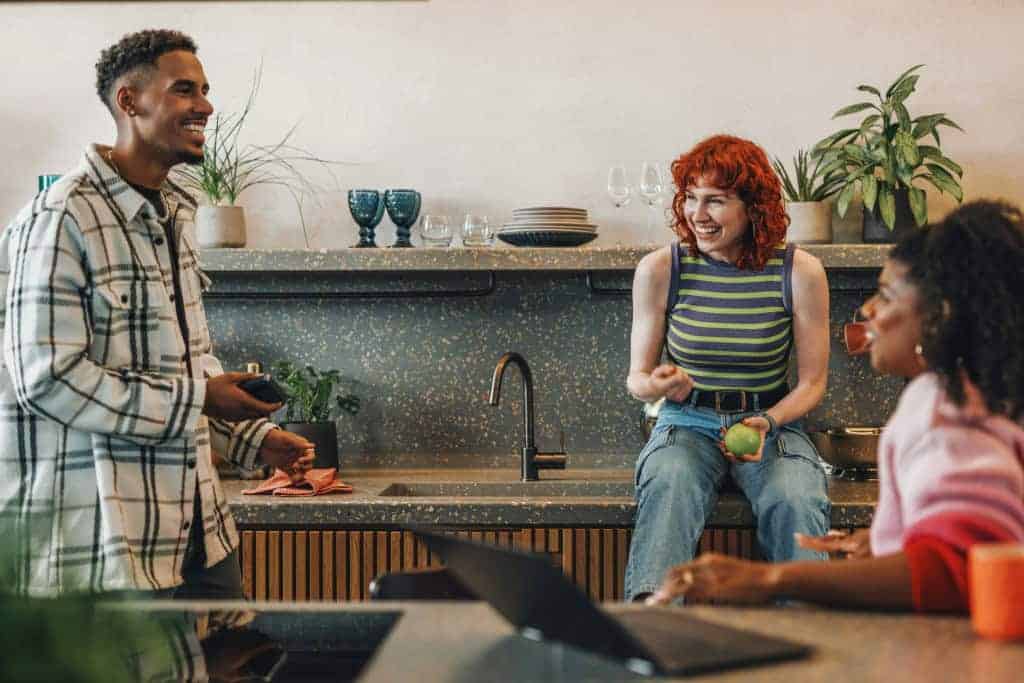 Three students sit around their rental apartment chatting. When considering between living on campus vs. off campus, they decided to rent an apartment off campus together.