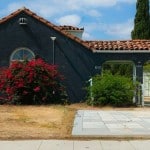 A Los Angeles stucco home painted a rich cobalt blue with a red tiled roof and big bushes out front.