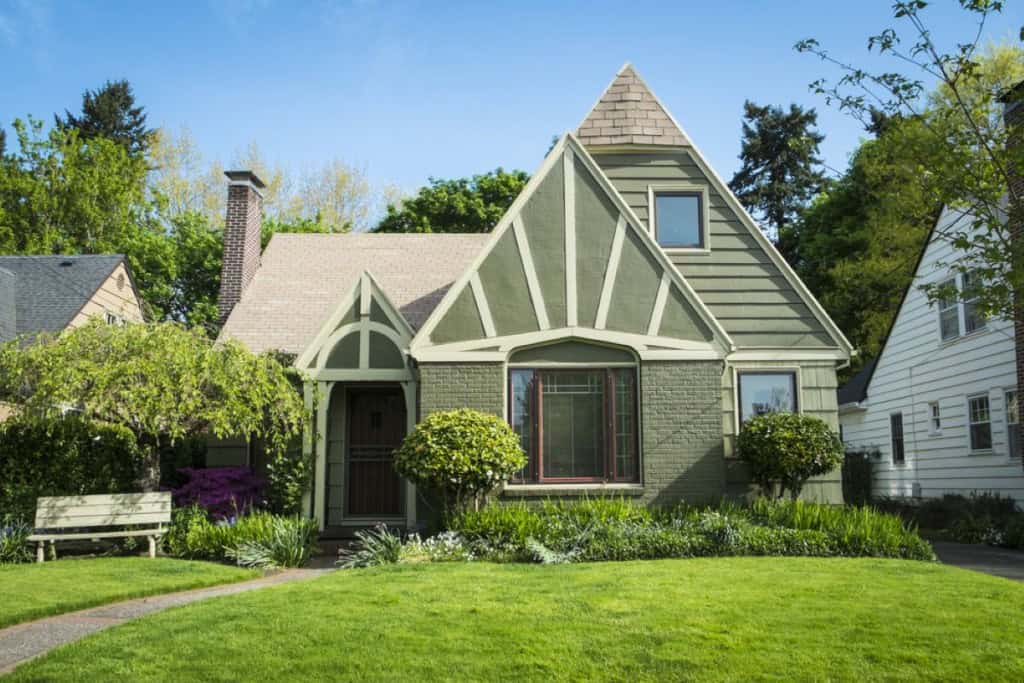 A bungalow style home, painted a soft green with white accents and a lush green lawn
