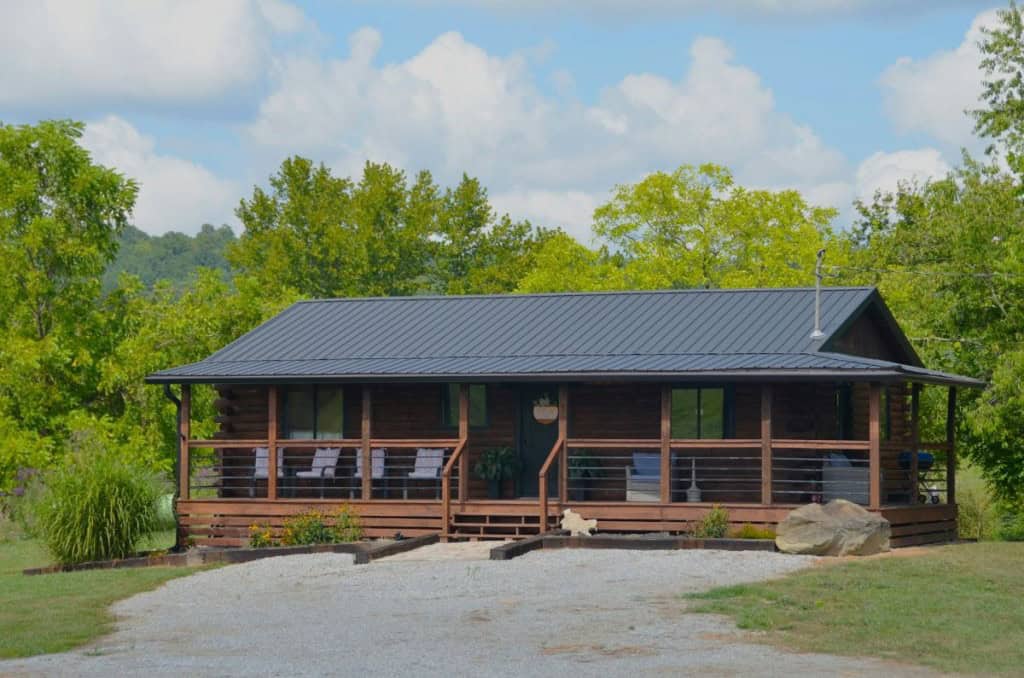 A modern mobile home with a wood deck and railing, set back in a forest