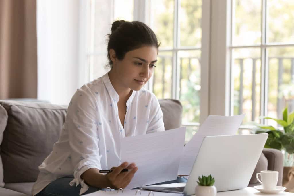 A young woman is researching documents and the internet to understand common first-time investor mistakes and how to avoid them.