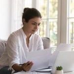 A young woman is researching documents and the internet to understand common first-time investor mistakes and how to avoid them.